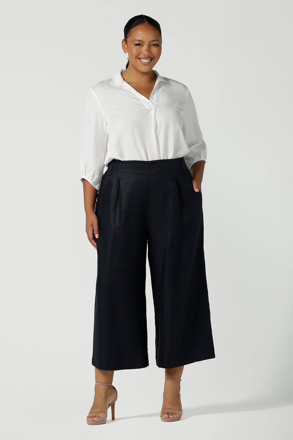 A corporate woman size 16 wears a linen Nik Pant in Midnight navy back with a white Arley shirt. A tailored pant with buttons and pleat front with a zip at the side. Petite height friendly. Linen fabric is a natural breathable material. Made in Australia for women size 8 - 24.