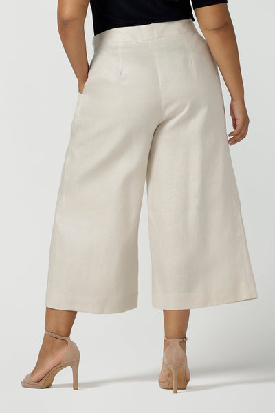 Close up of a size 16 woman wears the Nik Pant in Parchment Linen. A high waist tailored pant with buttons and pleats at the front. Made in natural linen a breathable fibre that is great for the warmer months. Styled back with a black Berni top. Made in Australia for women size 8 - 24.