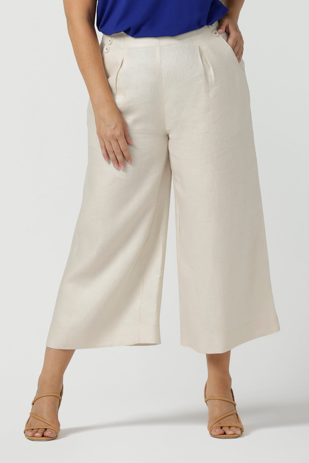 Close up of a size 12 woman wears the Nik Pant in Parchment Linen. A high waist tailored pant with buttons and pleats at the front. Made in natural linen a breathable fibre that is great for the warmer months. Styled back with a Cobalt Eddy Cami top. Made in Australia for women size 8 - 24.