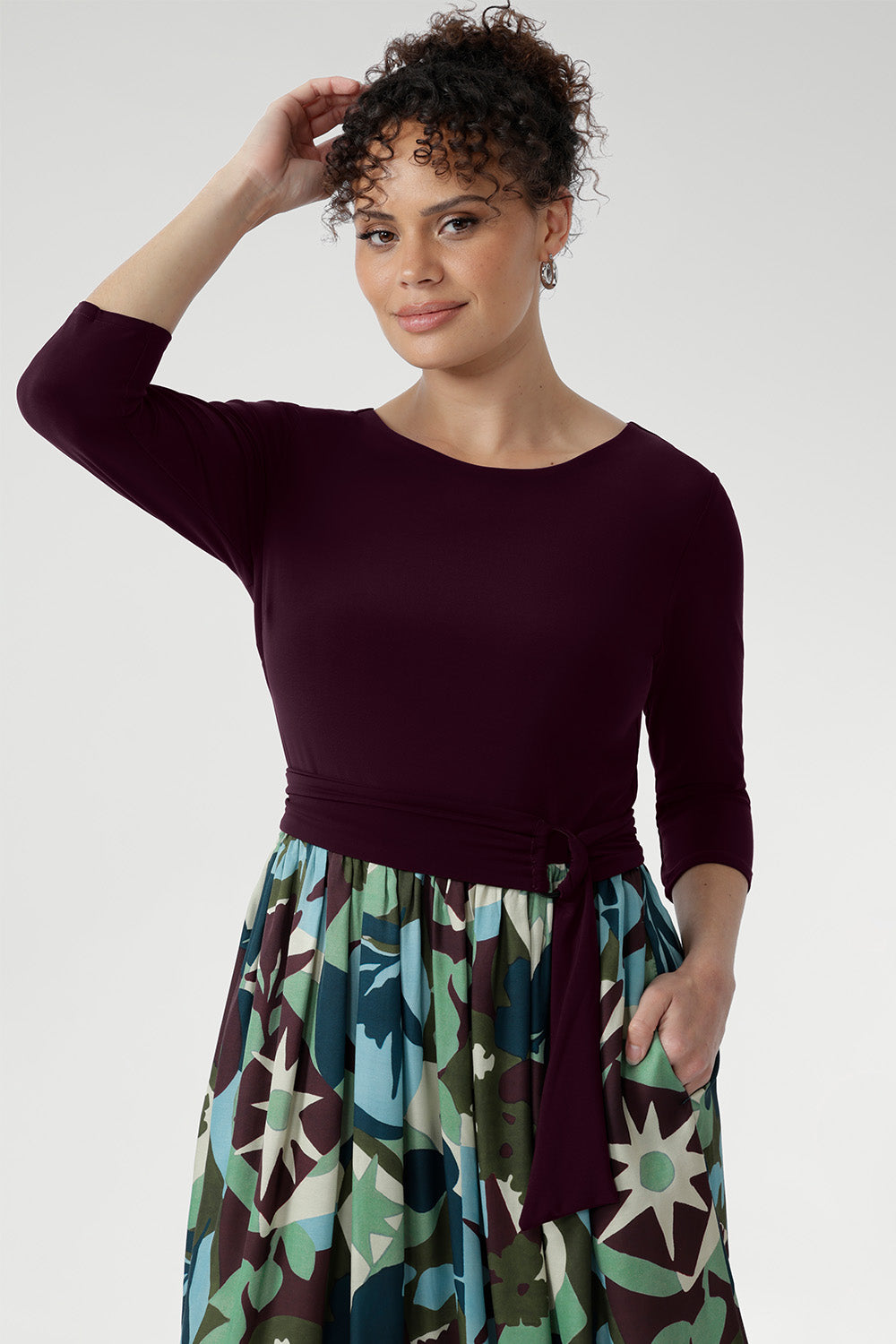 The flattering fit-and-flare silhouette is designed to suit all body shapes, with the option to wear it with or without its matching belt for versatile styling. A double-layered bodice offers added coverage and comfort, while ¾ sleeves and a gently rounded neckline create a refined, feminine finish. The midi-length A-line skirt features a bold abstract print in tones of green, blue, and plum—eye-catching yet timeless.