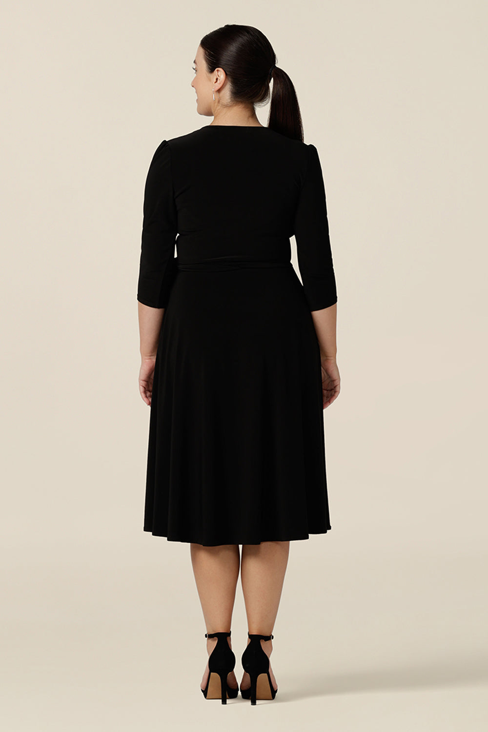 Back view of a knee length wrap dress in black jersey looking elegant as an evening and going out dress. Shown in size 10, this 3/4 sleeve event dress is made in Australia in dress sizes 8 to 24.