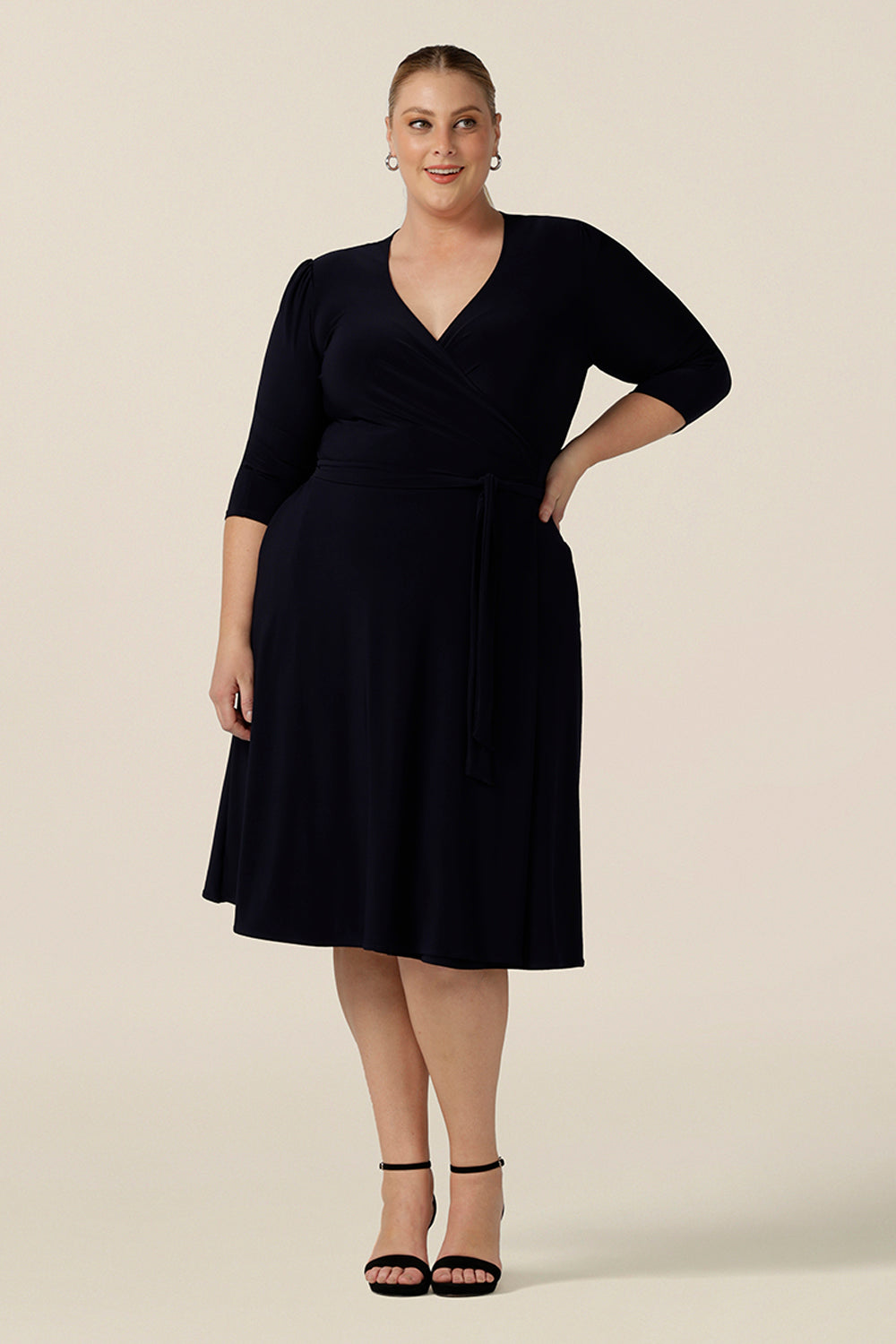 A classic knee length wrap dress in navy blue jersey looks elegant for evening and occasion wear. Shown on a fuller figure, size 18 woman, this plus size 3/4 sleeve event dress is made in Australia in dress sizes 8 to 24.
