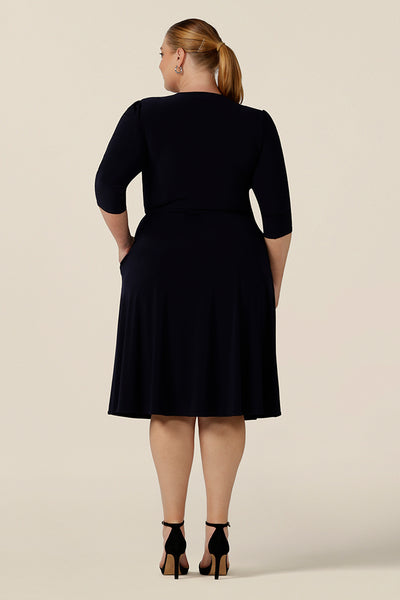 Back view of a knee length wrap dress in navy blue jersey looks elegant for evening and occasionwear. Shown for plus sizes, this 3/4 sleeve event dress is made in Australia in dress sizes 8 to 24.