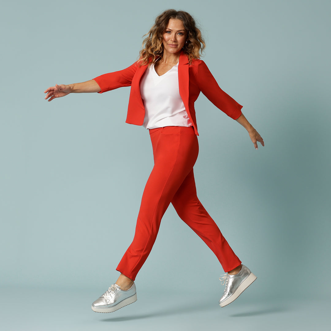 A tangerine red suit women will love, this images shows a an over 40 woman wearing a red suit set in a size 12. A tangerine red, 3/4 sleeve jacket for women is worn over a white bamboo jersey top and tapered leg, tangerine pants to create a full pant suit. MAde in Australia by Australian and New Zealand women's clothing brand, Leina & Fleur, shop this ladies suit set for work or casual wear in their online boutique.