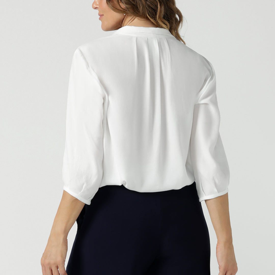 Showing the tailored details of a sustainable white shirt women will love. Made in Australia by Australian and New Zealand women's clothing brand, Leina & Fleur, this women's casual shirt has a pull-on V-neckline, back pleats and 3/4 sleeve. Available to buy in petite to plus sizes, shop this classic dress shirt in sizes 8 to 24.