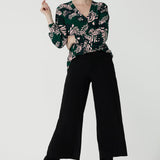 A size 10 woman wears the Paeton Top in  Alpine Fern. Styled back with the Bradley Pant in Black. A wide leg pant in black styled back with boots. Made in Australia for women size 8 - 24. 