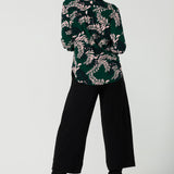 Back view of a size 10 woman wears the Paeton Top in Alpine Fern. Styled back with the Bradley Pant in Black. A wide leg pant in black styled back with boots. Made in Australia for women size 8 - 24.