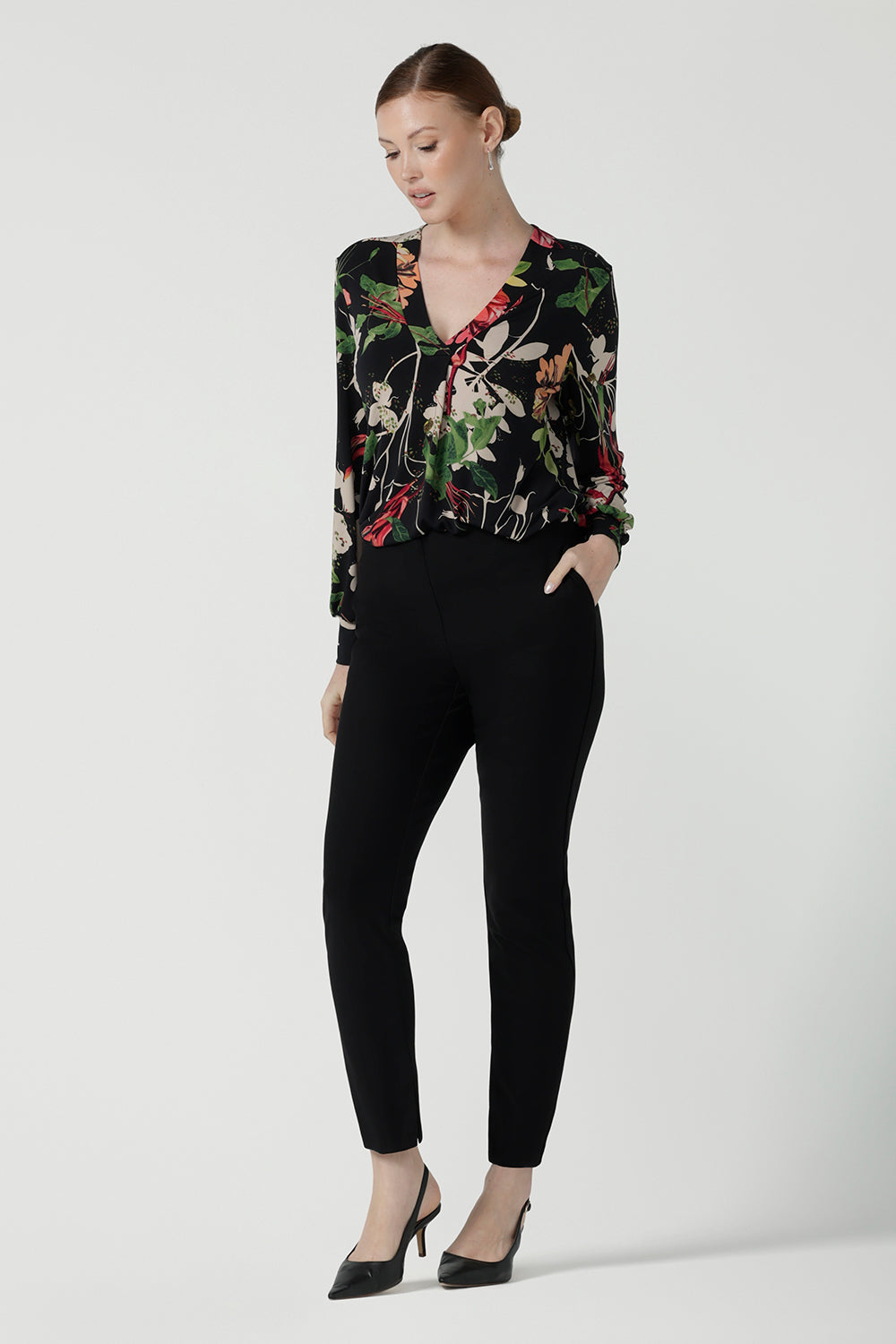 Front view of a size 10 woman wears a jersey work top called the Paeton in Bloomsbury print. Long sleeves with cuff detailed and made in Australia for women size 8-24. Styled back with slim fit comfortable work pants Broolyn in black.