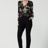 Front view of a size 10 woman wears a jersey work top called the Paeton in Bloomsbury print. Long sleeves with cuff detailed and made in Australia for women size 8-24. Styled back with slim fit comfortable work pants Broolyn in black.