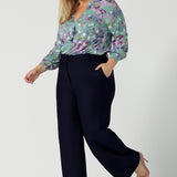 A size 18 woman wears the Kade tailored pant in Navy. Made in Australia for women size 8 - 24. Styled back with the Paeton top in day bloom. V-necline with pleat front and bind. Made in Australia for women size 8 - 24. 