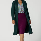 A size 10 woman wears the Andi skirt in Magenta. A made in Australia skirt styled back with the Paeton top in Day Bloom and the Sorel Trenchcoat in green. Size 8 - 24.