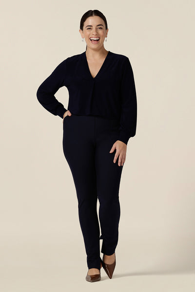 A woman wears a V-neck, long sleeve jersey top in navy blue with slim leg trousers in navy blue easy care jersey. Made in Australia by women's clothing label, Leina & Fleur, this great work top is available to shop online in sizes 8 to 24.