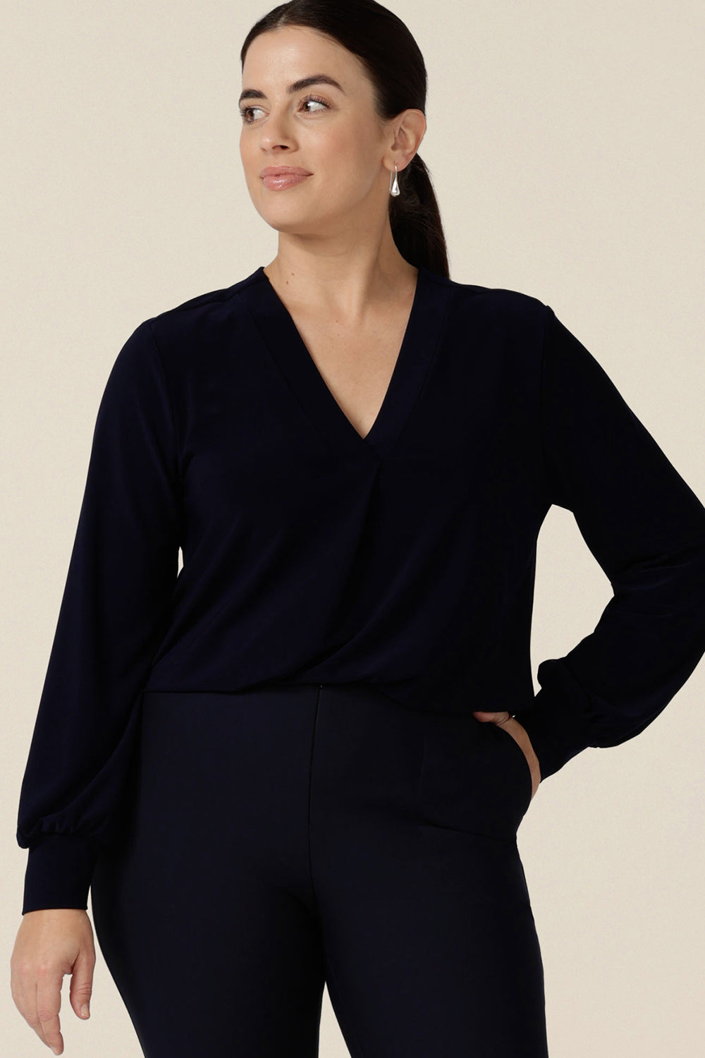 A woman wears a V-neck, long sleeve jersey top in navy blue. Made in Australia by women's clothing label, Leina & Fleur, this great work top is available to shop online in sizes 8 to 24.