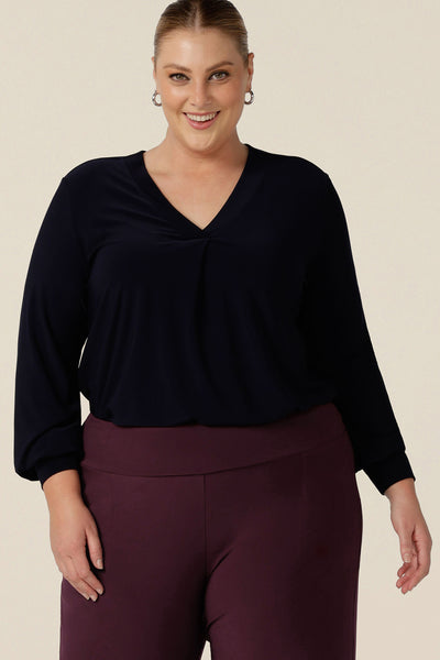 A woman wears a V-neck, long sleeve jersey top in navy blue, size 18. Made in Australia by women's clothing label, Leina & Fleur, this great work top is available to shop online in sizes 8 to 24, petite to plus sizes.
