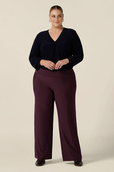 A woman wears a V-neck, long sleeve jersey top in navy blue, size 18 with mulberry red stretch jersey, wide leg pants for work. Made in Australia by women's clothing label, Leina & Fleur, this great work top is available to shop online in sizes 8 to 24, petite to plus sizes.