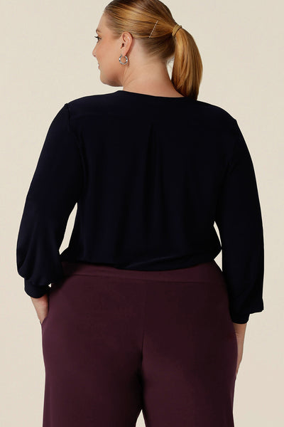 Back view of a woman wearing a V-neck, long sleeve jersey top in navy blue, size 18. Made in Australia by women's clothing label, Leina & Fleur, this great work top is available to shop online in sizes 8 to 24, petite to plus sizes.