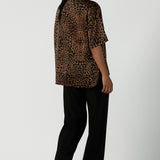 A back view of a woman wearing the Pele Shirt in Bronze Animal, a satin shirt with a relaxed dropped shoulder and fashionable leopard print animal design. Made in Australia for women size 8-24.