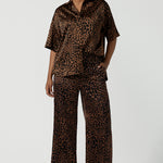 A woman wears the Sloane Pant in Bronze Animal. A satin straight leg waisted pant with pockets and a zip front. Made in high fashion Animal print fabric. Petite to plus size women size 8-24. Styled back with the Pele Shirt in Bronze animal.
