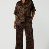 A woman wears the Sloane Pant in Bronze Animal. A satin straight leg waisted pant with pockets and a zip front. Made in high fashion Animal print fabric. Petite to plus size women size 8-24. Styled back with the Pele Shirt in Bronze animal.