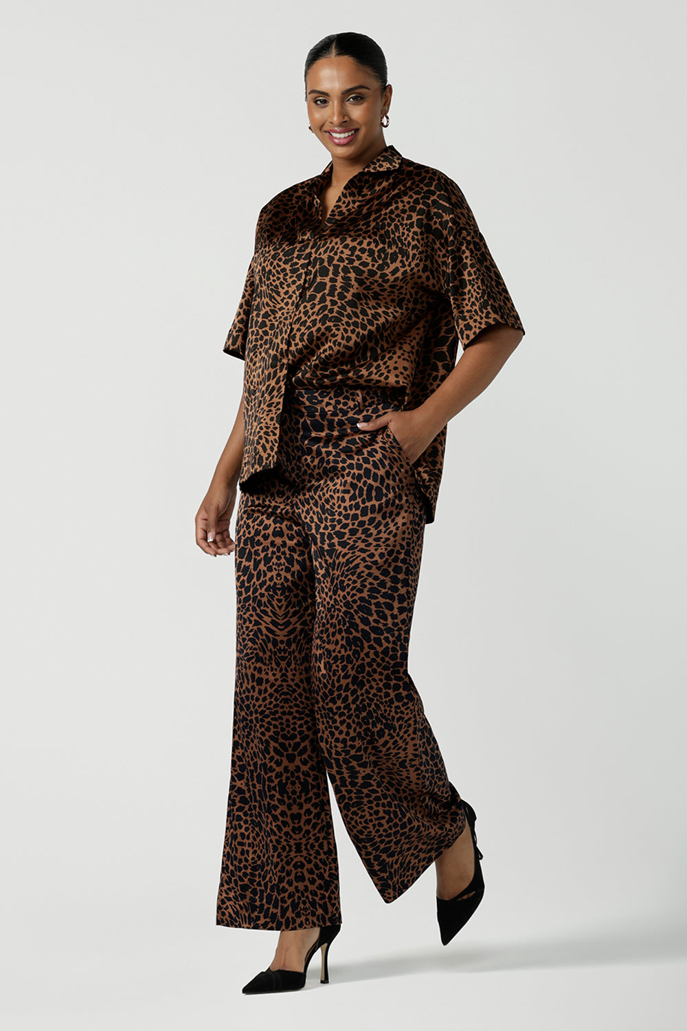 A woman wears the Pele Shirt in Bronze Animal, a satin shirt with a relaxed dropped shoulder and fashionable leopard print animal design. Made in Australia for women size 8-24. Paired back with a matching pair of the Sloane Pant in Bronze Foil.