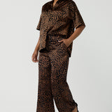 A woman wears the Pele Shirt in Bronze Animal, a satin shirt with a relaxed dropped shoulder and fashionable leopard print animal design. Made in Australia for women size 8-24. Paired back with a matching pair of the Sloane Pant in Bronze Foil.