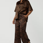 A woman wears the Sloane Pant in Bronze Animal. A satin straight leg waisted pant with pockets and a zip front. Made in high fashion Animal print fabric. Petite to plus size women size 8-24. Styled back with the Pele Shirt in Bronze animal.