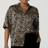 A woman wears the Pele Shirt in Animal print satin. A Australian made shirt with fashionable leopard print on a black base with vanilla spots. Made in Australia style for women petite to plus size 8-24.