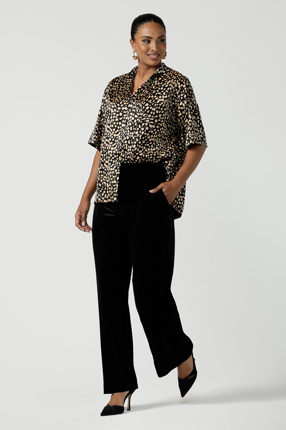 A woman wears the Pele Shirt in Animal print satin. A Australian made shirt with fashionable leopard print on a black base with vanilla spots. Made in Australia style for women petite to plus size 8-24. Styled back with Black monroe pants for women.