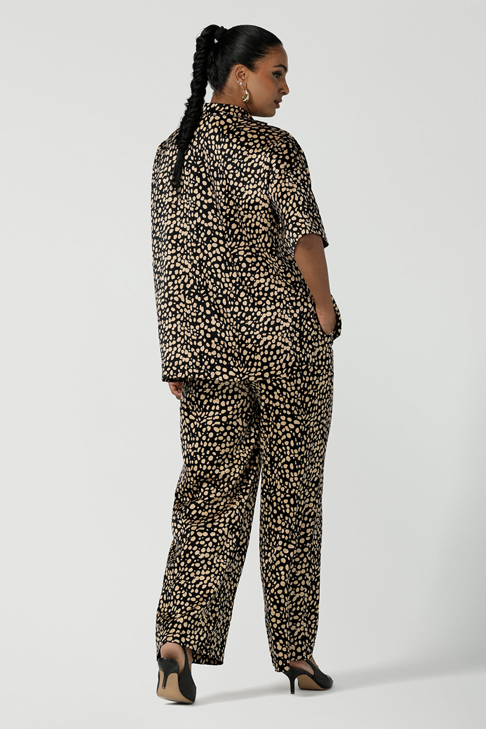 Back view of a woman wears the Pele Shirt in Animal print satin. A Australian made shirt with fashionable leopard print on a black base with vanilla spots. Made in Australia style for women petite to plus size 8-24. Styled back with matching straight leg satin pants.