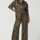 A woman wears the Pele Shirt in Animal print satin. A Australian made shirt with fashionable leopard print on a black base with vanilla spots. Made in Australia style for women petite to plus size 8-24. Styled back with matching straight leg satin pants.