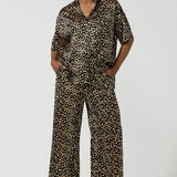 A woman wears the Pele Shirt in Animal print satin. A Australian made shirt with fashionable leopard print on a black base with vanilla spots. Made in Australia style for women petite to plus size 8-24. Styled back with matching straight leg satin pants.