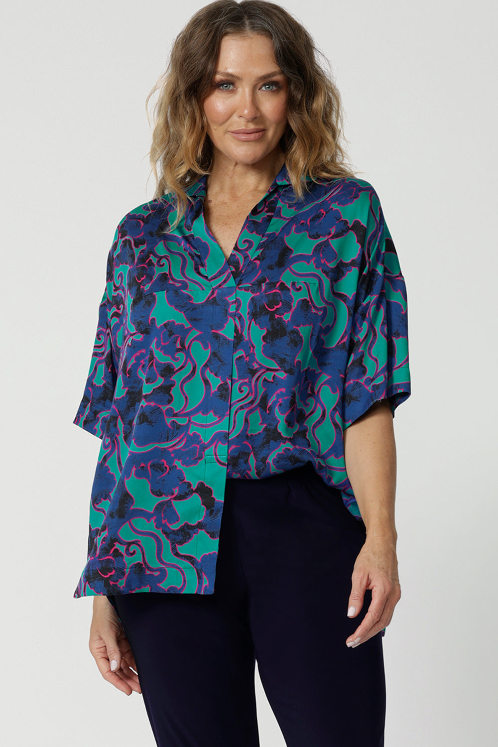 Close up front on image of 40y/o woman wearing a brightly coloured shirt  made of comfortable satin rayon material. The abstract design has colours of aqua, pink and cobalt blue. Lightweight shirt is Australian made by women from Australia and New Zealand. Leina and Fleur is a woman’s clothing label that proudly stocks both plus and petite sizes, with sizes ranging from 8 to 24. 