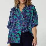 Close up front on image of 40y/o woman wearing a brightly coloured shirt  made of comfortable satin rayon material. The abstract design has colours of aqua, pink and cobalt blue. Lightweight shirt is Australian made by women from Australia and New Zealand. Leina and Fleur is a woman’s clothing label that proudly stocks both plus and petite sizes, with sizes ranging from 8 to 24. 