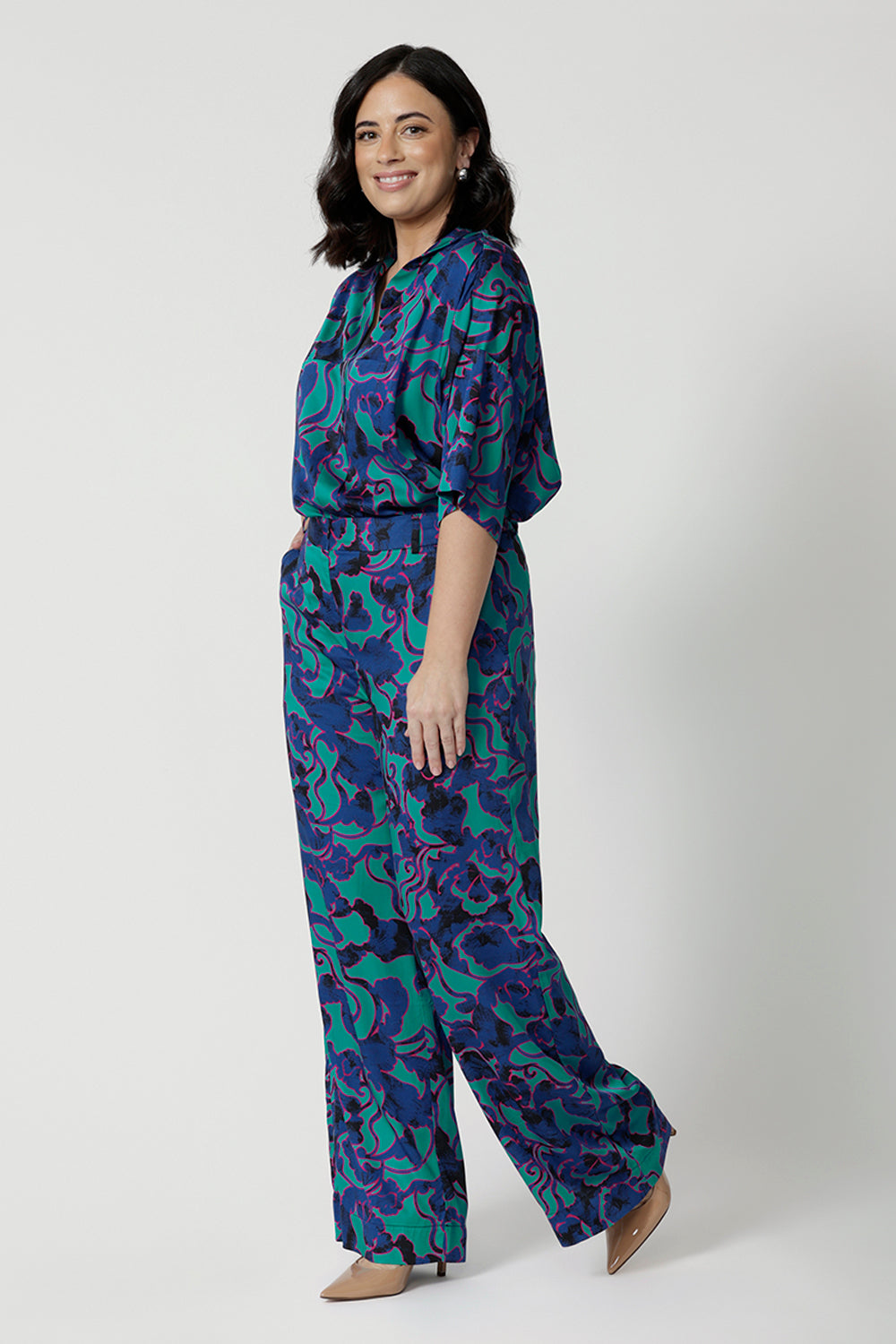 Image of a petite woman wearing a matching Jade Deco Shirt and pant set. This lightweight, above elbow-length shirt has and an abstract pattern displaying navy, pink and aqua blue colours. This Australian made shirt and pant set is made of satin rayon fabric that is breathable and comfortable. Leina & Fleur is a women’s clothing company that actively stocks plus & petite sizes ranging from 8 to 24.