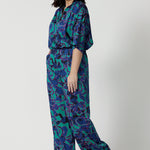 Full body shot image of a petite female model, wearing a matching light weight shirt and pant set. The abstract design of the set displays navy, pink and aqua blue colours. This Australian made shirt and pant set is made from satin rayon fabric that is breathable and comfortable. Leina and Fleur is a women’s clothing company that actively stocks plus sizes & petite sizes ranging from 8 to 24.