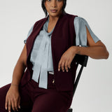 Fitted vest made from a luxe Scuba Crepe Jersey fabric that offers a soft, textured feel with full body stretch, ensuring comfort and flexibility throughout the day. Size 10 model wears her vest unzipped over blue blouse. Shop the Pennyworth Vest for a sophisticated stretch suit ensemble. Available in Sizes 8-24.