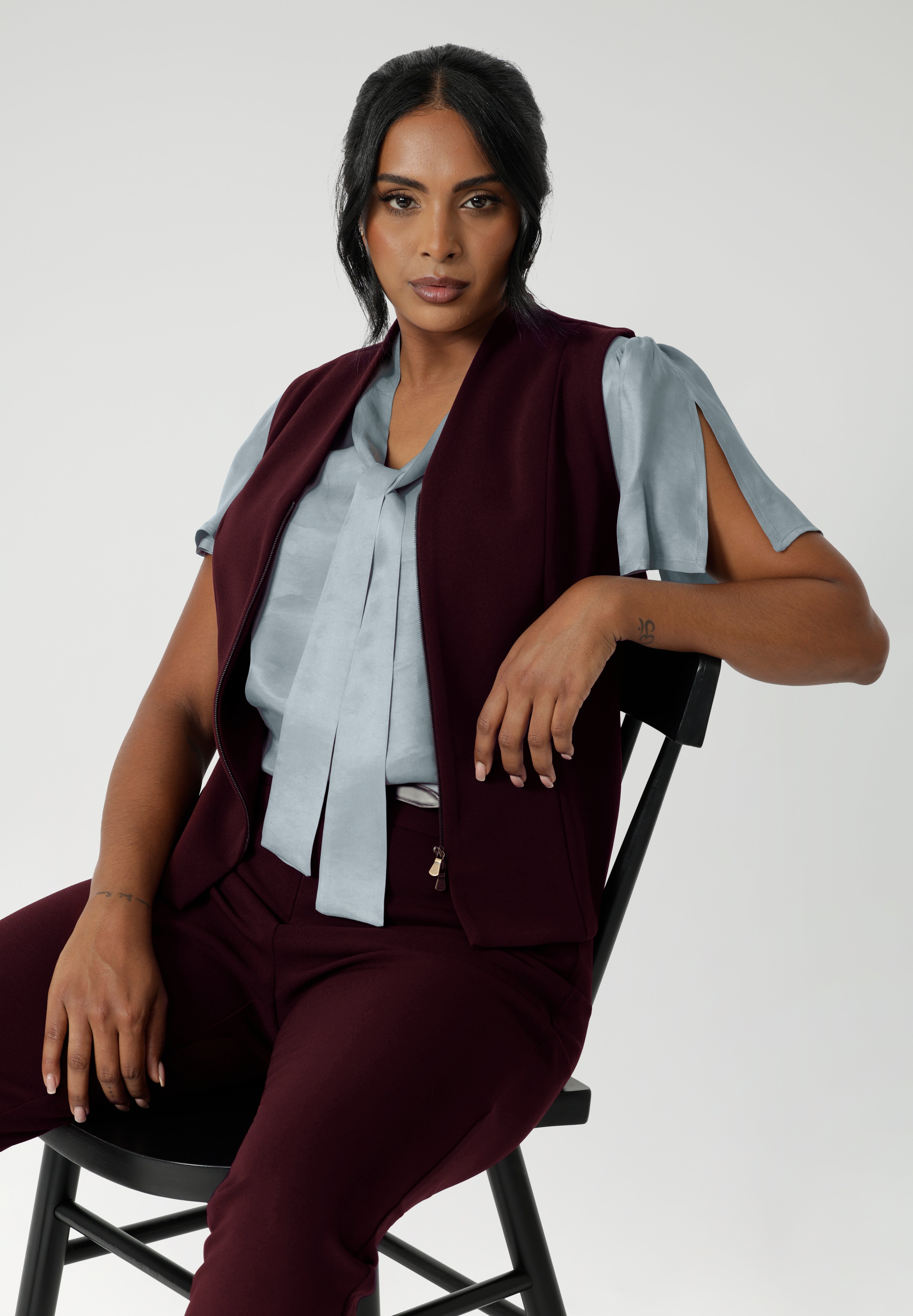 Fitted vest made from a luxe Scuba Crepe Jersey fabric that offers a soft, textured feel with full body stretch, ensuring comfort and flexibility throughout the day. Size 10 model wears her vest unzipped over blue blouse. Shop the Pennyworth Vest for a sophisticated stretch suit ensemble. Available in Sizes 8-24.