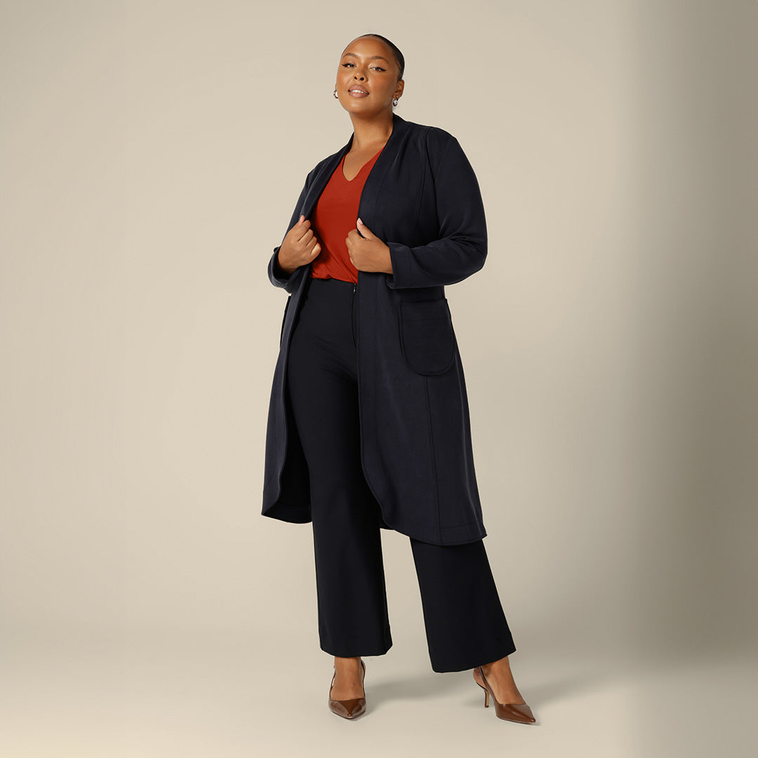 A plus size, size 18 woman wears a blue trenchcoat, orange work top and plus size tailored work pants to highlight a good fashion brand for plus size pants for women. Australian plus size fashion brand, Leina & Fleur makes quality trousers for plus size women - shop these work pants in sizes 8 to 24.