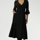 Size 10 corporate woman wears the Portia dress in Black. A wrap dress in black with tie side and 3/4 sleeve. Styled with long brown boots. Made in Australia for women size 8 - 24.