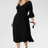 Size 18 corporate woman wears the Portia dress in Black. A midi length wrap dress in black with a side tie and 3/4 sleeve. Made in Australia for women size 8 - 24.