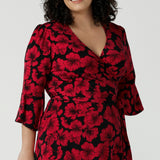 Close up of a size 18 woman wears the Portia dress in Bold Poppy. Red floral dress with flutter sleeves and a black base. Made in Australia for women size 8 - 24.