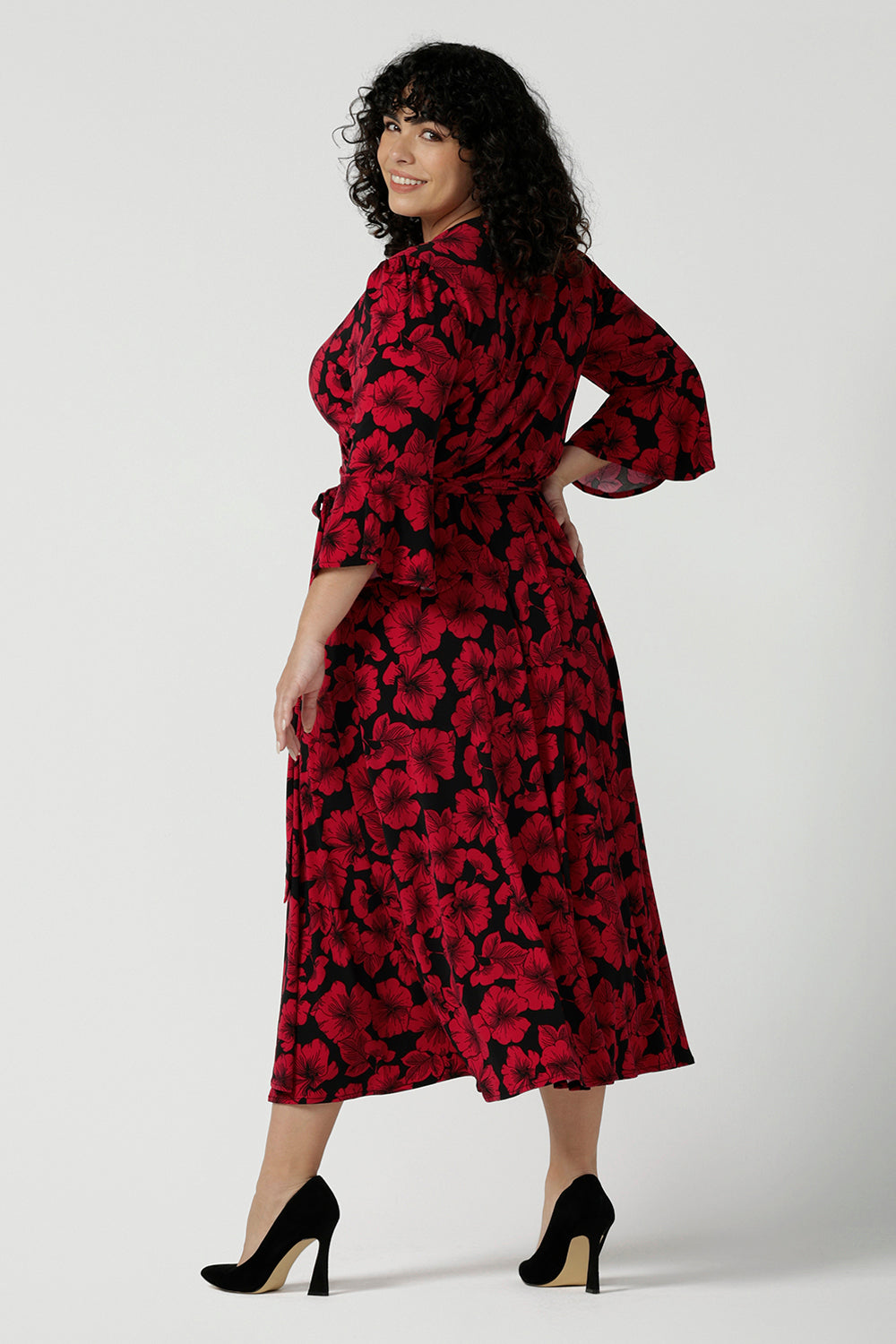 Back view of a size 18 woman wears the Portia dress in Bold Poppy. Red floral dress with flutter sleeves and a black base. Made in Australia for women size 8 - 24.