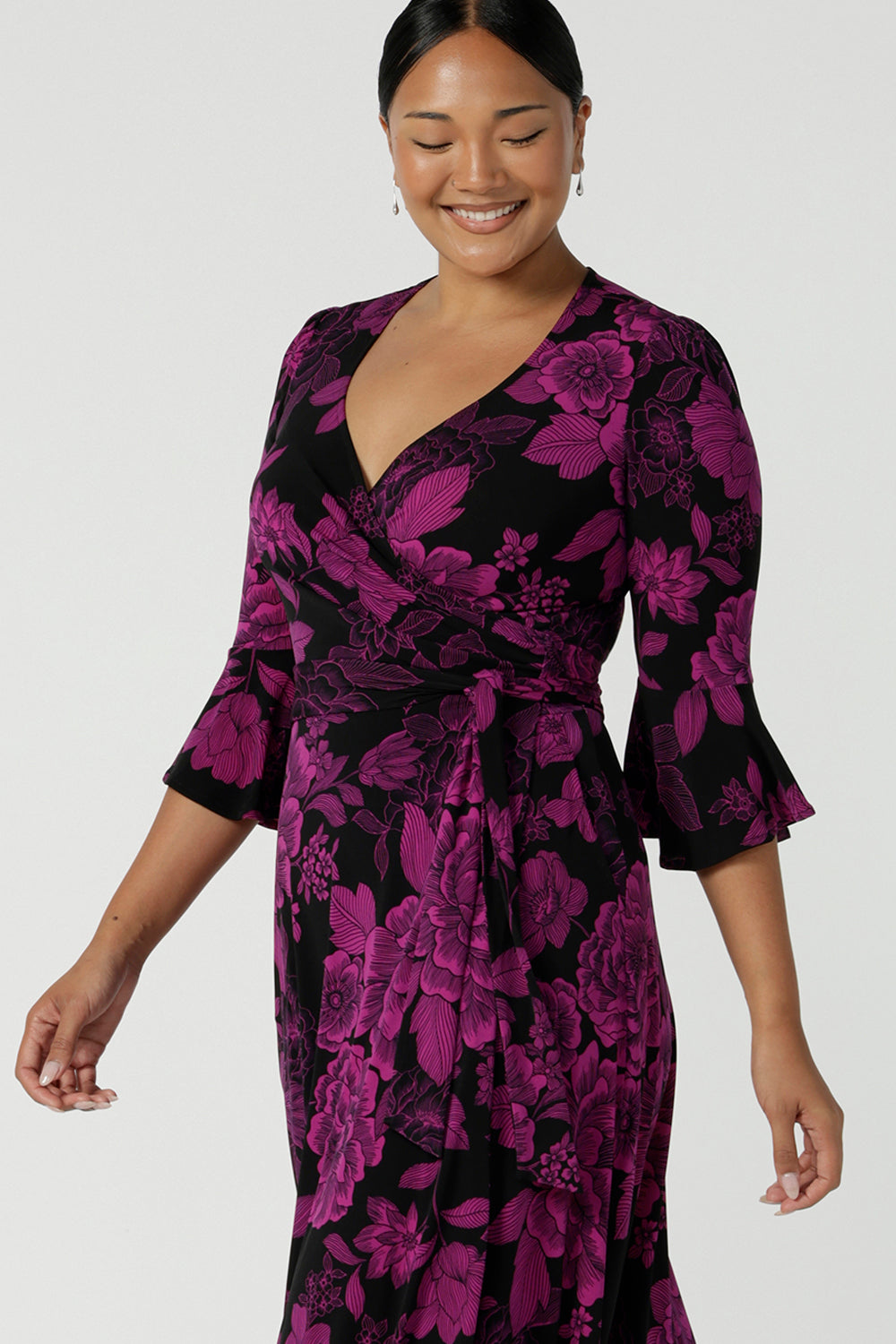 A close up of a Size 10 woman wears the Portia Wrap dress in Fuchsia Flora. Portia in Fuchsia Flora is a below the knee length wrap dress with pockets. Our signature fluted sleeve detail gives her a romantic feel. Made in Australia for women size 8 - 24.