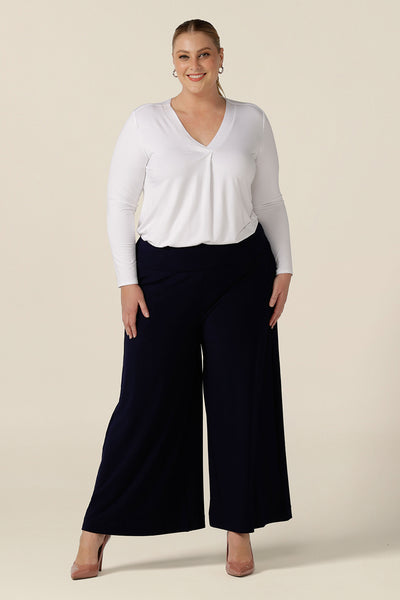 A plus size, size 18 woman wears navy blue wide leg pants with pockets with a white bamboo jersey top. These pull-on, easy care pants are comfortable for your everyday workwear capsule wardrobe. Shop these Australian-made navy trousers online in sizes 8 to 24, petite to plus sizes.