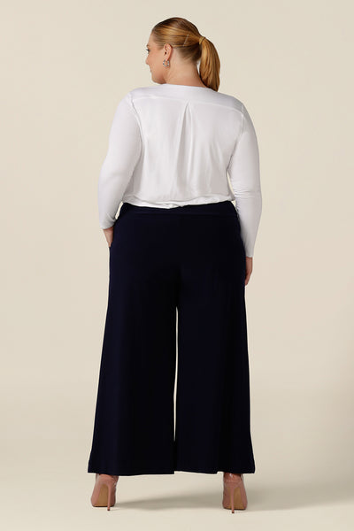 Back view of a plus size, size 18 woman wearing navy blue wide leg pants with pockets with a white bamboo jersey top. These pull-on, easy care pants are comfortable for your everyday workwear capsule wardrobe. Shop these Australian-made navy trousers online in sizes 8 to 24, petite to plus sizes
