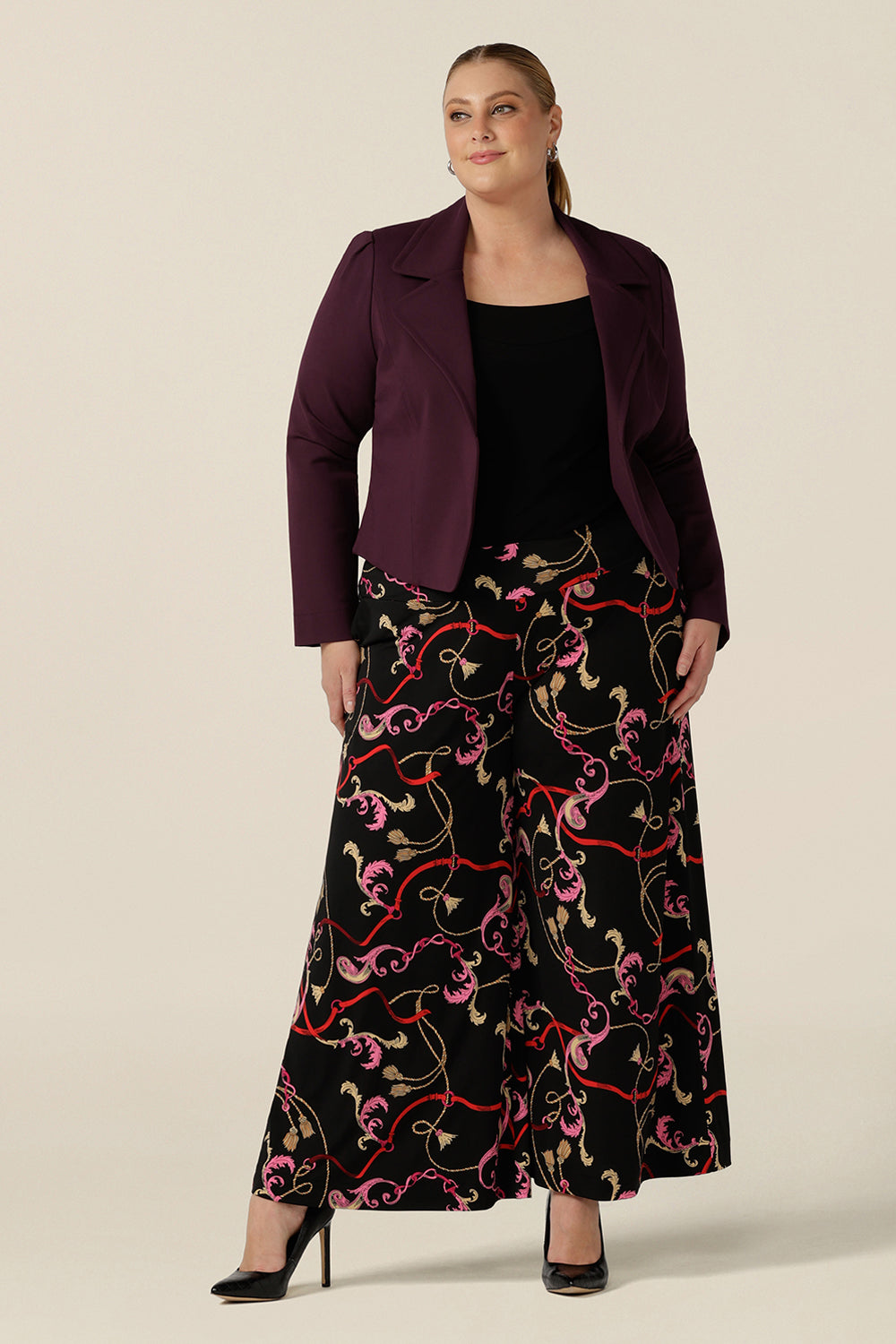 A fuller figure, size 18 woman wears printed wide leg pants with pockets with a square neck black top and tailored work jacket in mulberry red. These pull-on, easy care pants are comfortable for your everyday workwear capsule wardrobe. Shop these Australian-made wide leg trousers online in sizes 8 to 24, petite to plus sizes.