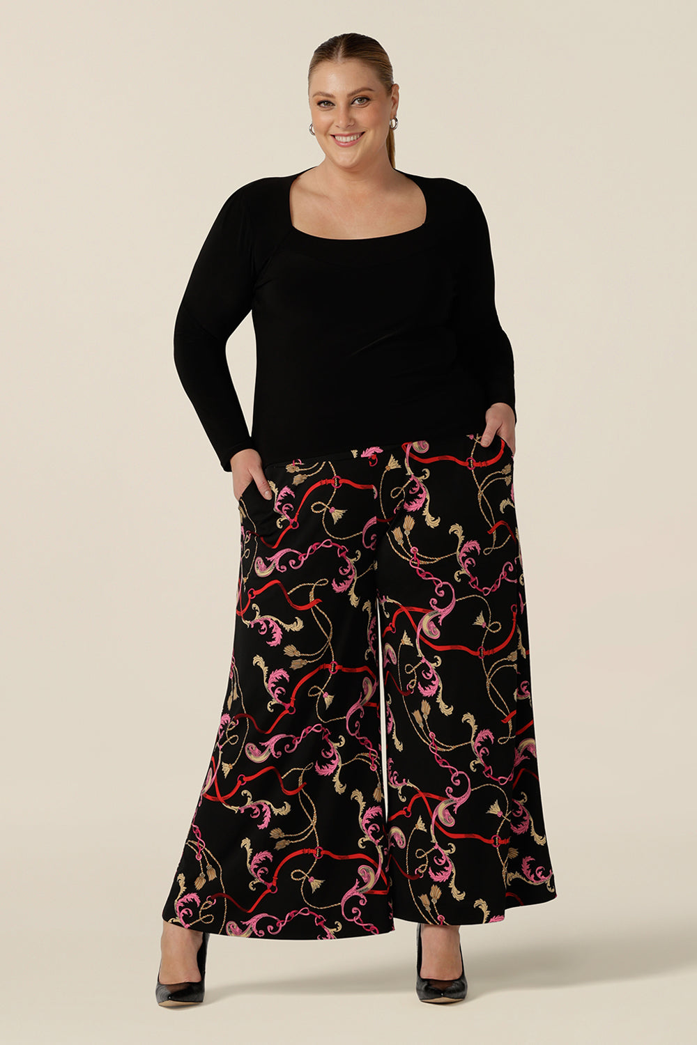 A plus size, size 18 woman wears printed wide leg pants with pockets with a square neck long sleeve black top. These pull-on, easy care pants are comfortable for your everyday workwear capsule wardrobe. Shop these Australian-made wide leg trousers online in sizes 8 to 24, petite to plus sizes.