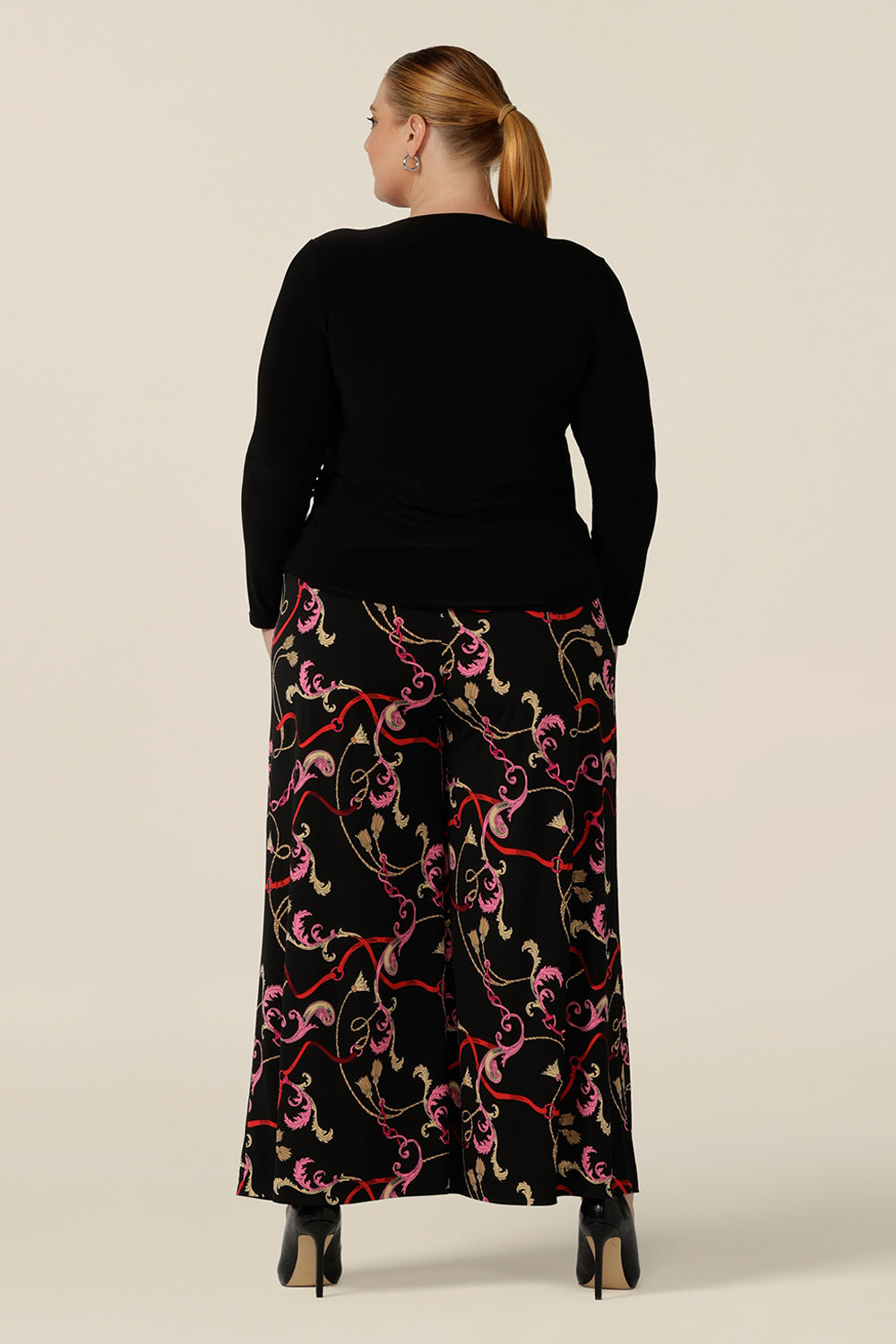 Back view of a plus size, size 18 woman wearing printed wide leg pants with pockets and a long sleeve black top. These pull-on, easy care pants are comfortable for your everyday workwear capsule wardrobe. Shop these Australian-made wide leg trousers online in sizes 8 to 24, petite to plus sizes.