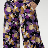 The vibrant painterly-style floral print in rich purples and soft yellow hues adds an artistic edge, making these pants perfect for travel, special occasions, or simply turning heads wherever you go.