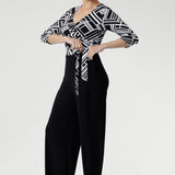 Showcasing a striking black and white geometric print across the wrap-style bodice, this jumpsuit features a flattering self-tie waist and a double-layered back for a refined and supportive fit. 